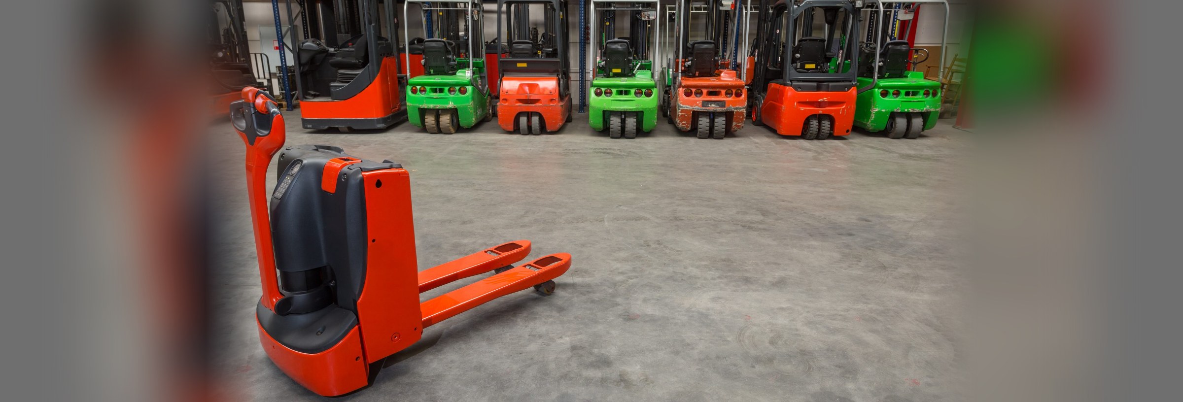 Forklifts and pallet jack machines lined up in a warehouse.