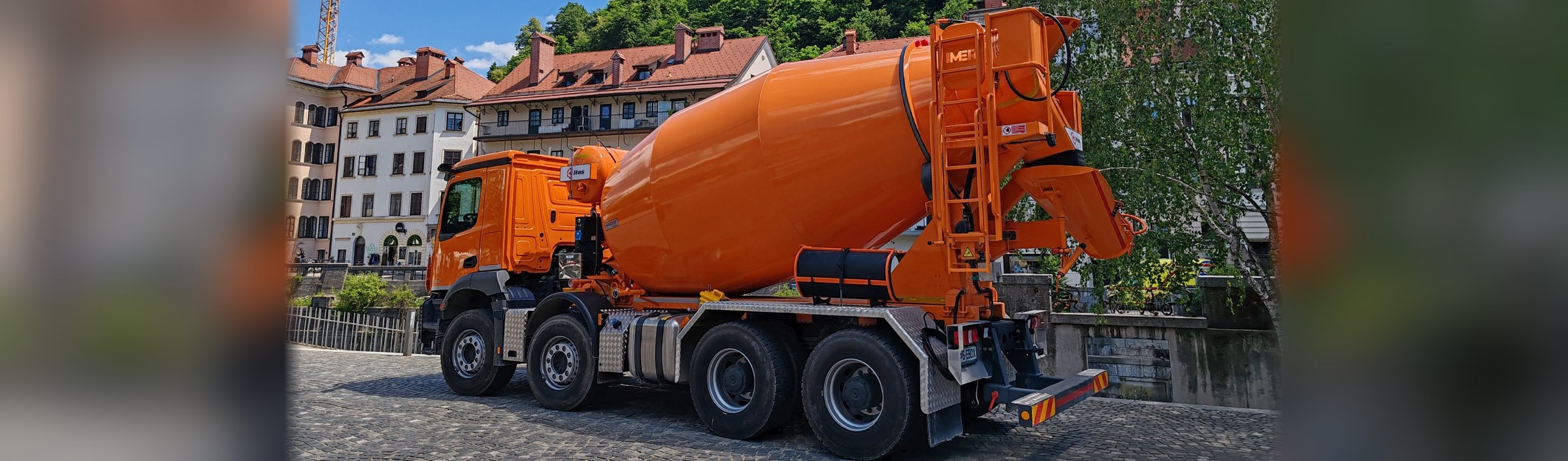 A ready-mix concrete truck parked on a cobbled street, drum and chute raised, wheels on the ground.