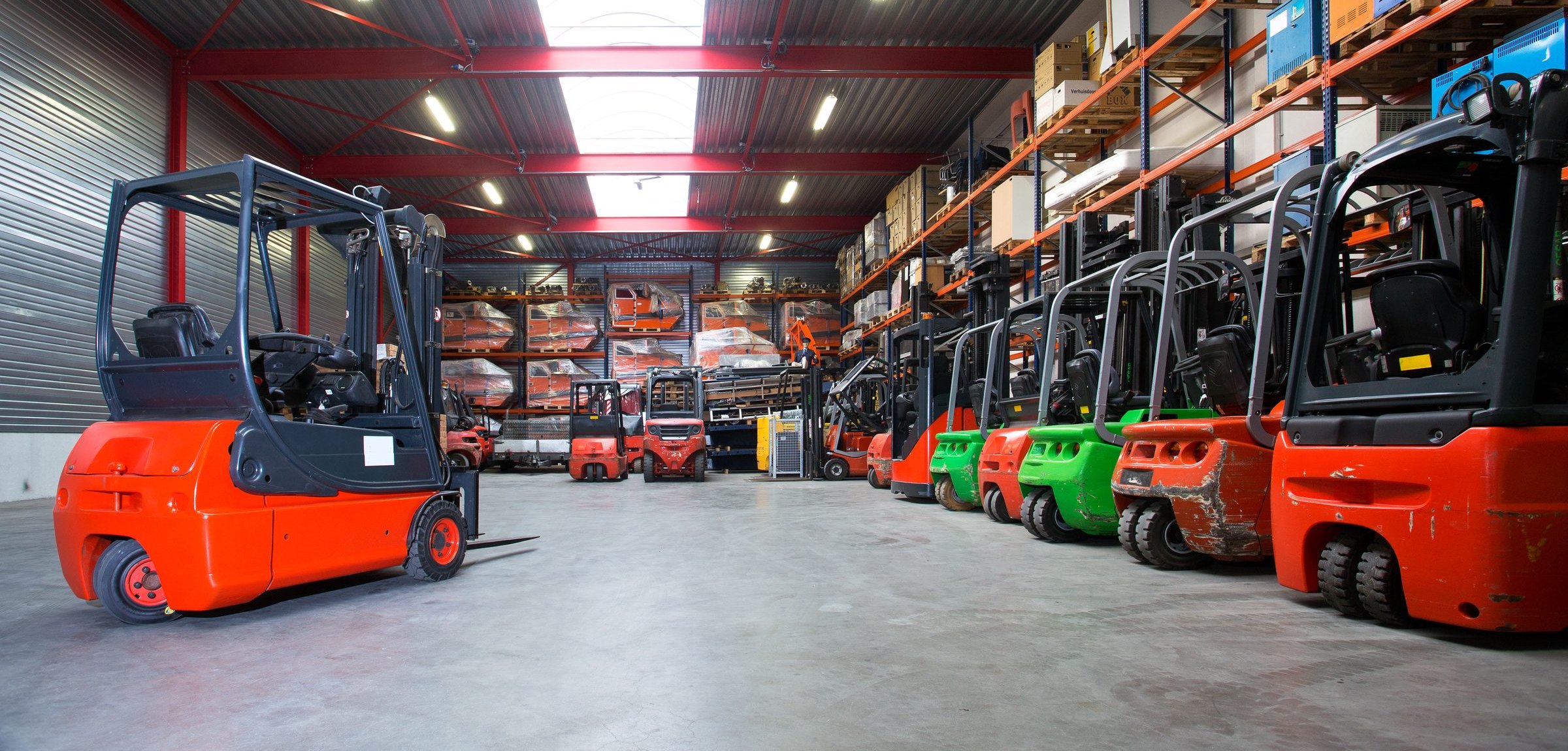 A fleet of electric counterbalance forklifts parked in rows inside a warehouse.