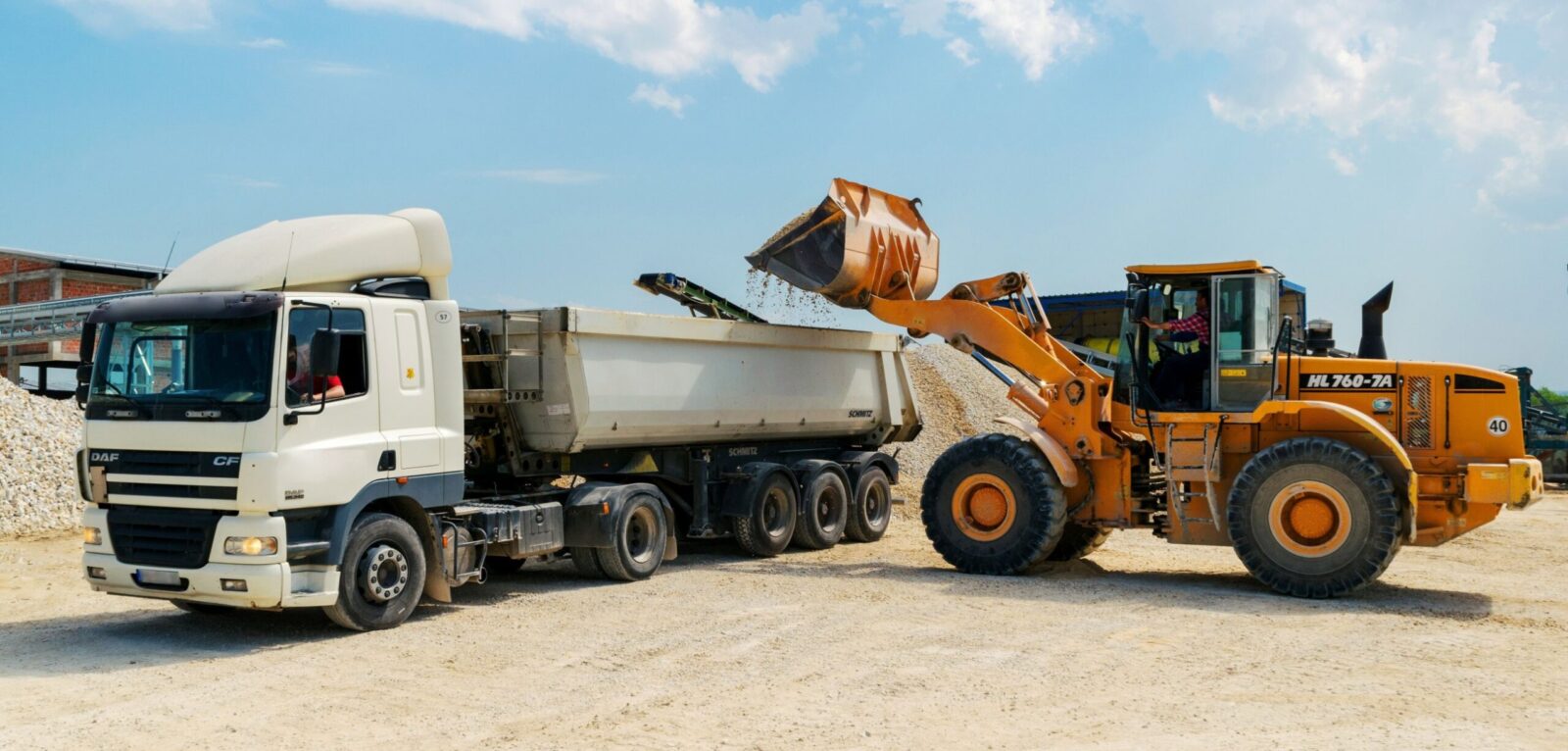 A wheel loader tipping crushed aggregate into the body of a tipper trailer at an aggregates yard.